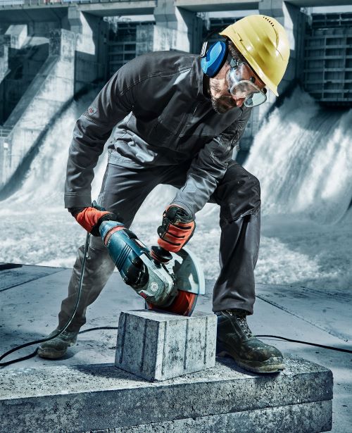 Ein Mann flext einen Stein in robuster Arbeitshose.